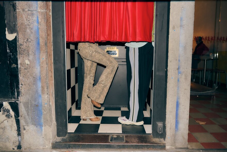 A vintage-style photo booth with red curtains and two sets of legs visible underneath them.