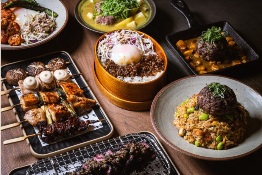 Array of Japanese teppanyaki dishes on a table including meat and rice, skwers and soup.