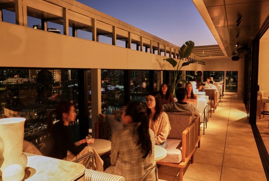 Patrons enjoying the atmosphere at a rooftop bar, with city lights at night behind them.