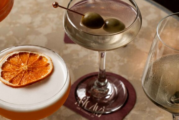 Looking down at a table at a martini cocktail and a frothy orange coloured cocktail.