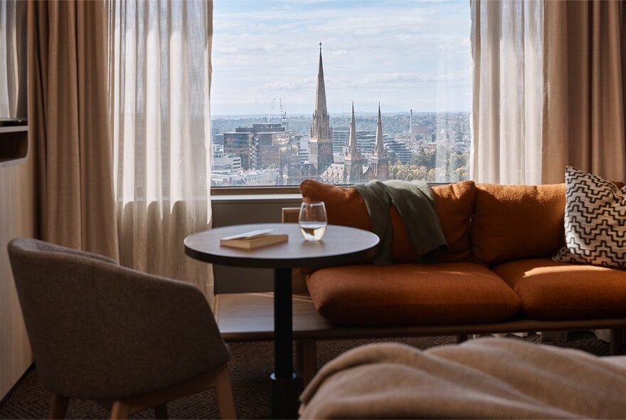 Hotel room with views of St Patrick's Cathedral through a window with drapes, sofa, chair and table in the foreground.