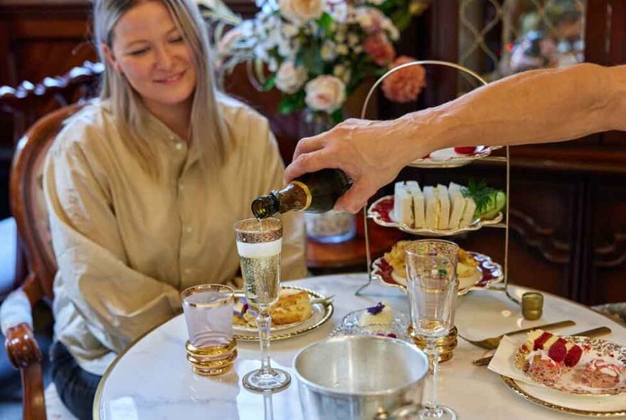 A woman sitting at a table enjoying high tea with champagne.