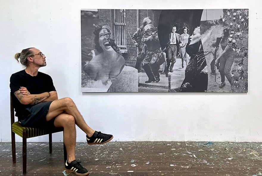 Artist seated in front of a collage artwork.