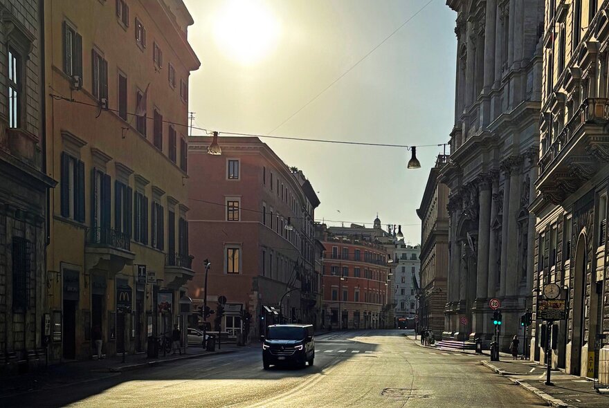 View of a street in Rome on a bright sunny morning, with a single car on the road.