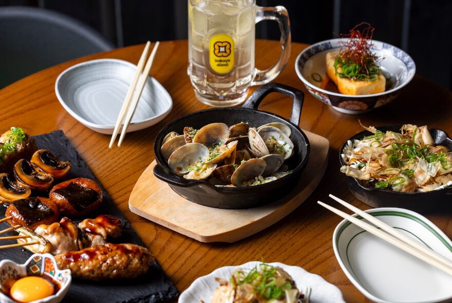 A selection of Japanese dishes presented on a wooden table alongside two empty plates with chopsticks lying on top.