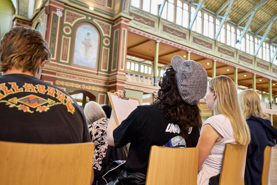 People seated in chairs in the great exhibition space in the Royal Exhibition Building, Melbourne.