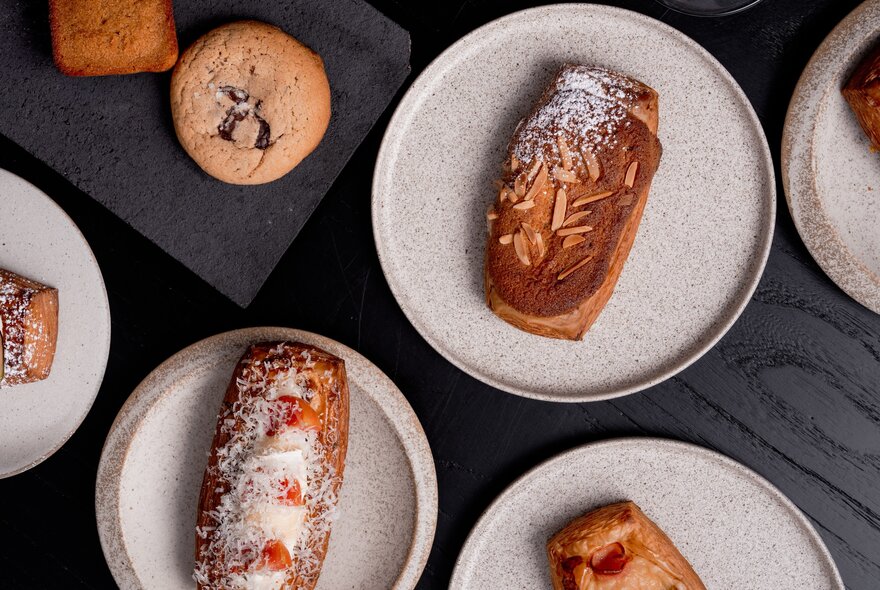 Plates of pastries and cookies on a dark table.