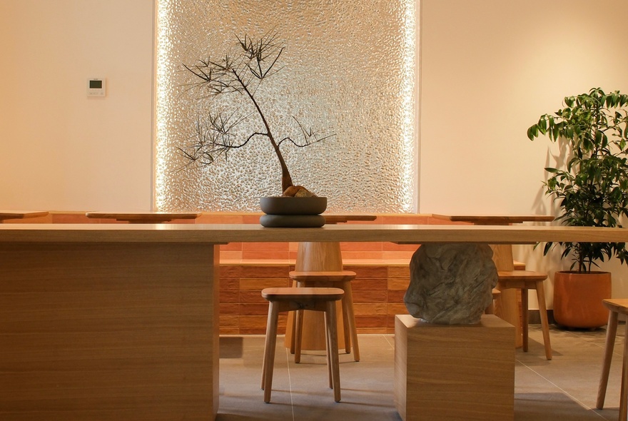 Tranquil low-lit seating area with bonsai plants and simple wooden furniture.