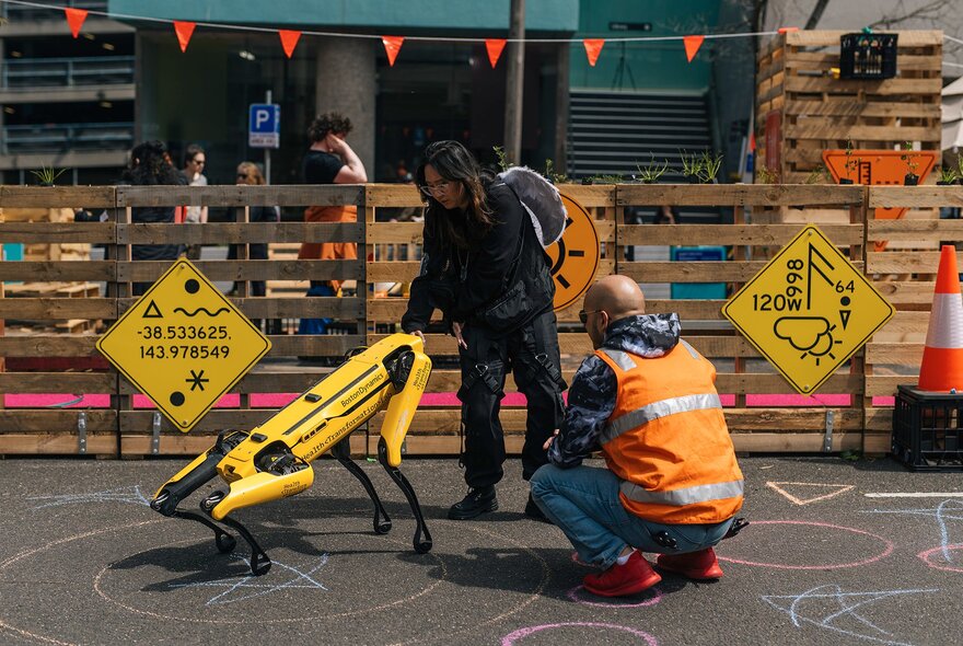 Game participants looking at a robot creature near packing case fences.