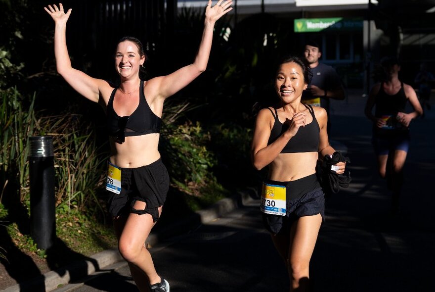 Two runners at night with their arms raised in the air.