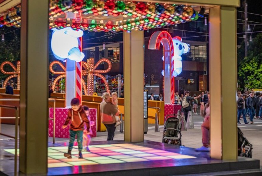 Kids dancing on a coloured light-up dance floor with Christmas decorations all around. 