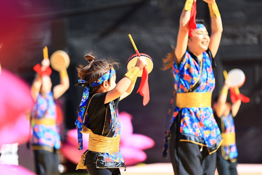 Children dressed in Japanese matsuri outfits, holding drums.