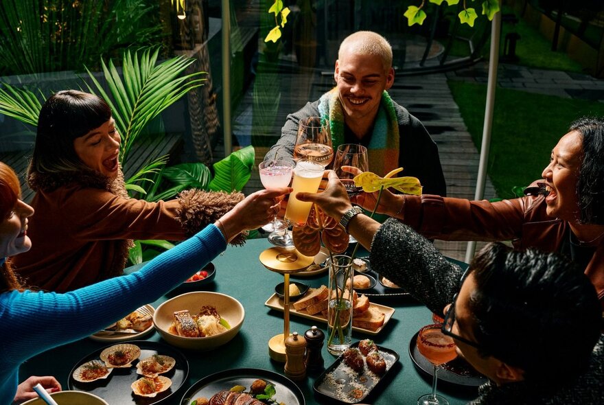People seated at a table clinking drinks over plates of food.