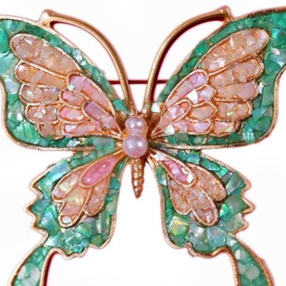 A butterfly brooch with green and pink mother of pearl inlay wings, against a white background.