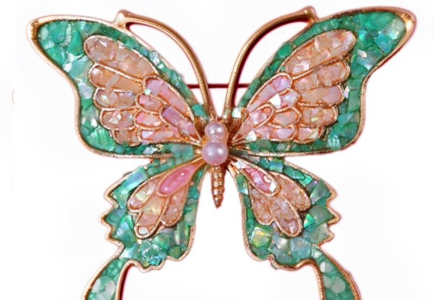 A butterfly brooch with green and pink mother of pearl inlay wings, against a white background.