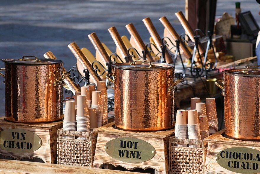 Three copper pots of wine with paper cups stacked in between them.