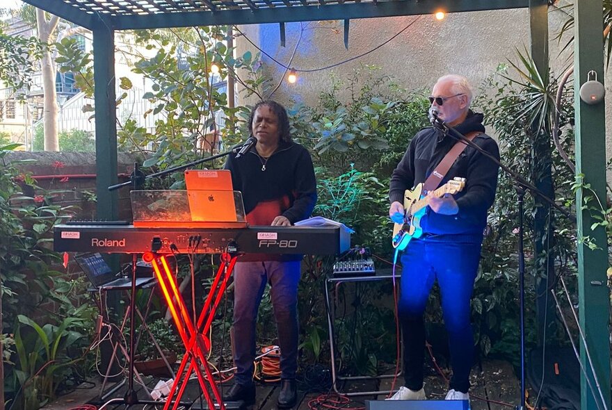 Soul musician Dinash Daniel playing the keyboard in an outdoor setting with a guitarist.