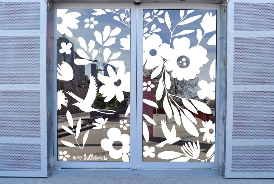 A doorway with sliding glass doors featuring white cut out mural artwork on the glass inspired by Australian native flora and fauna.