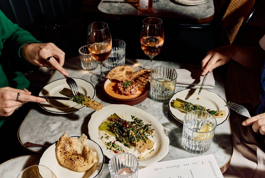 Looking down on a dinner table with people eating and glasses of rose and water.