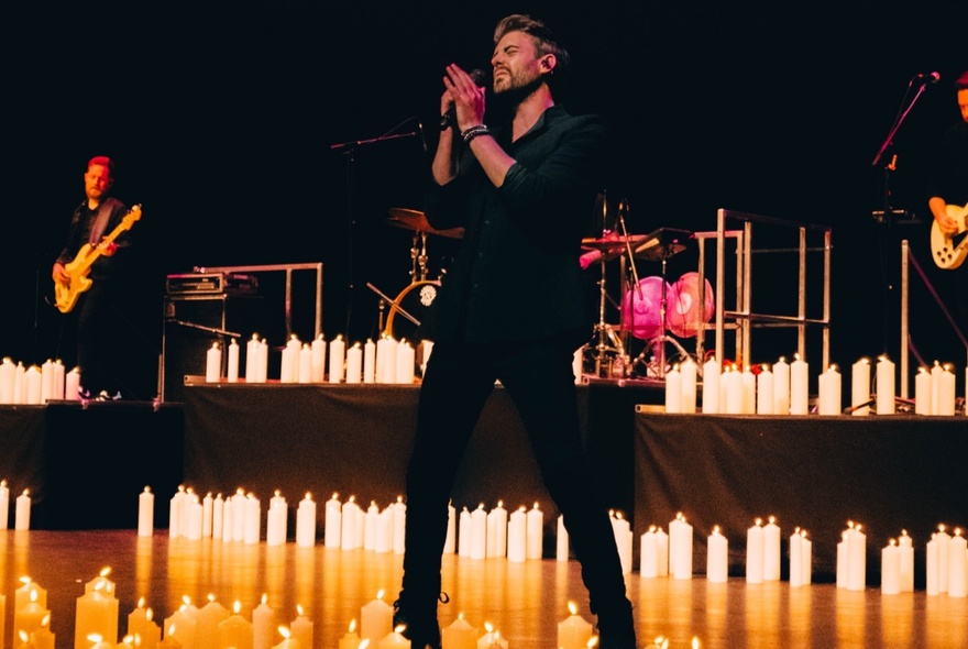 A man singing on a candlelit stage, musicians playing behind him.