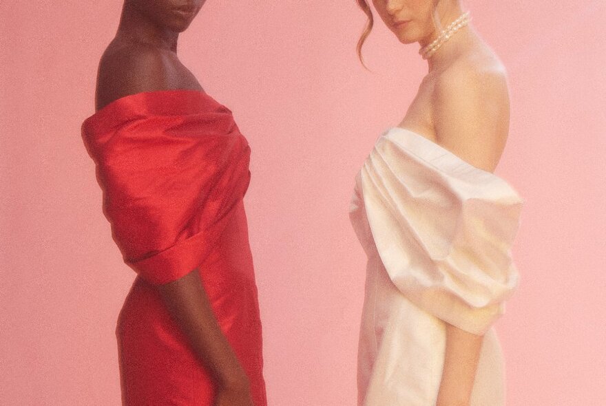 Two models wearing strapless dresses, one red and one off-white, facing each other in profile. 