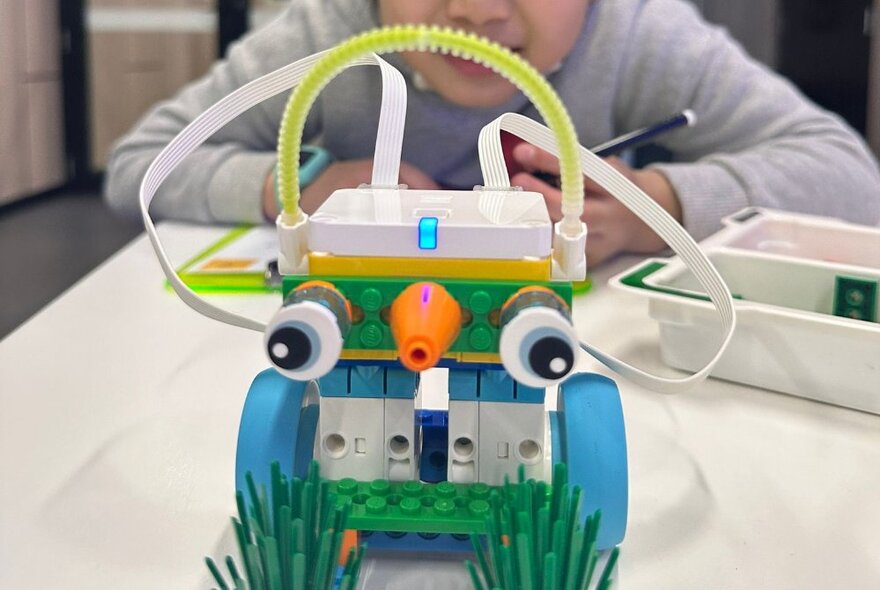 A child seated at a table looking at a robotic toy made from Lego.