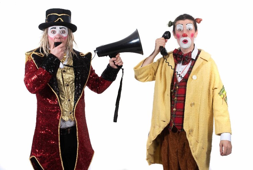 Two performers dressed in circus style costumes and wearing face paint, one holding a megaphone and the other an old fashioned telephone handset.