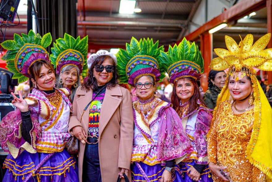 A group of Filipino women in colourful traditional dress, posing with a woman in a brown coat.