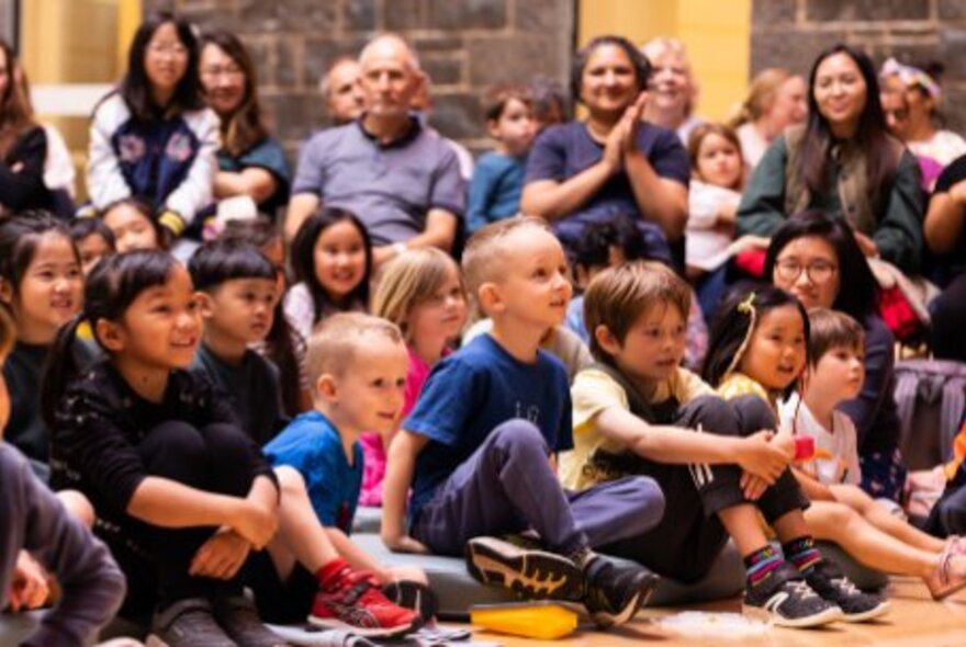 Group of children seated on the floor while adults look on.