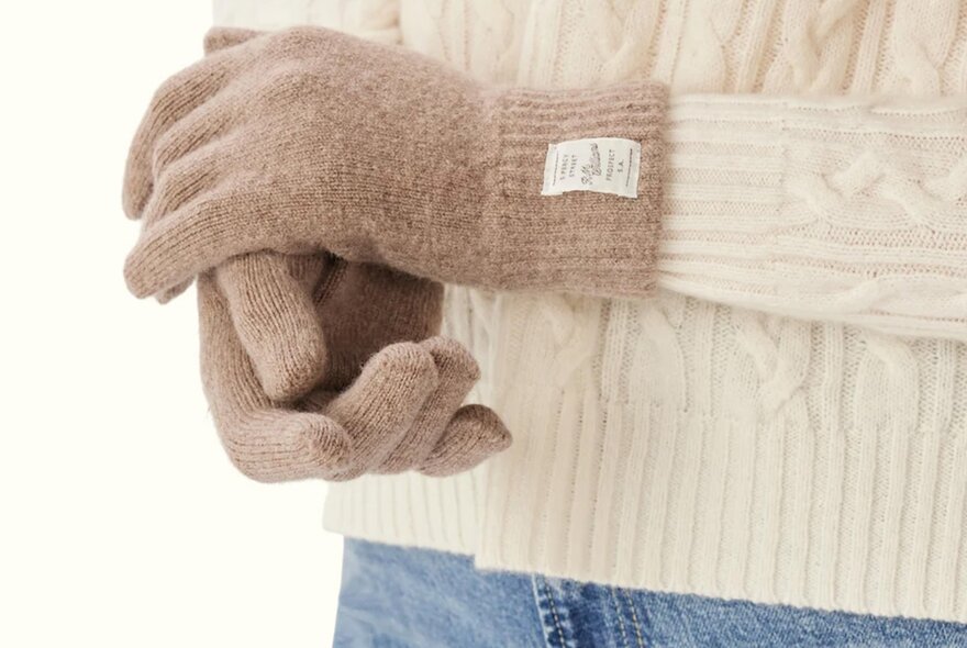A person is wearing a pair of beige wool gloves.