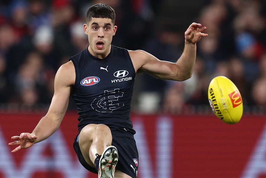Carlton AFL football player kicking the ball during a match.