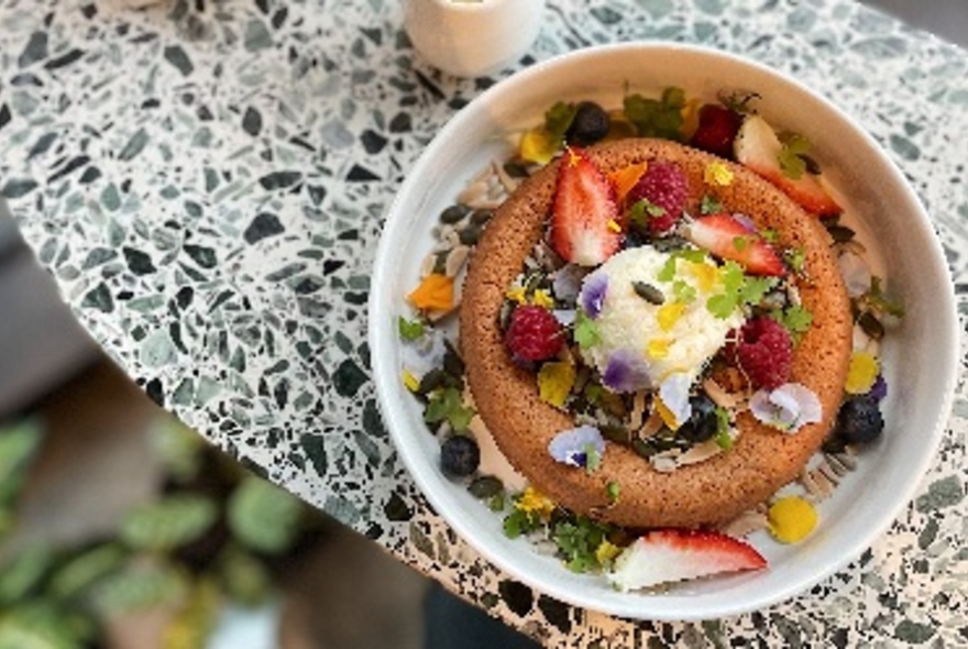 Pastry topped with fruit and leaves in white bowl on green marble-look surface.