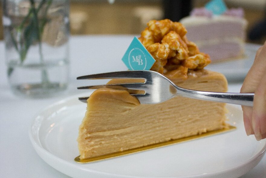 A person cutting into a salted caramel layered crepe cake with a dessert fork.