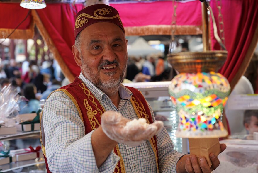 A man in traditional Turkish clothing holding out his hand. 