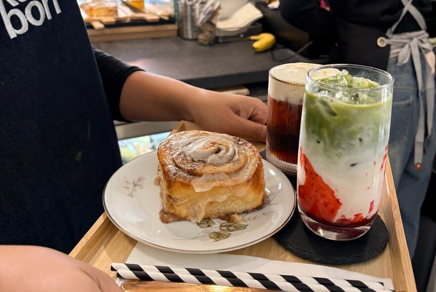 Kids hands holding a cafe tray with a cinnamon bun, mont blanc coffee and matcha drink.