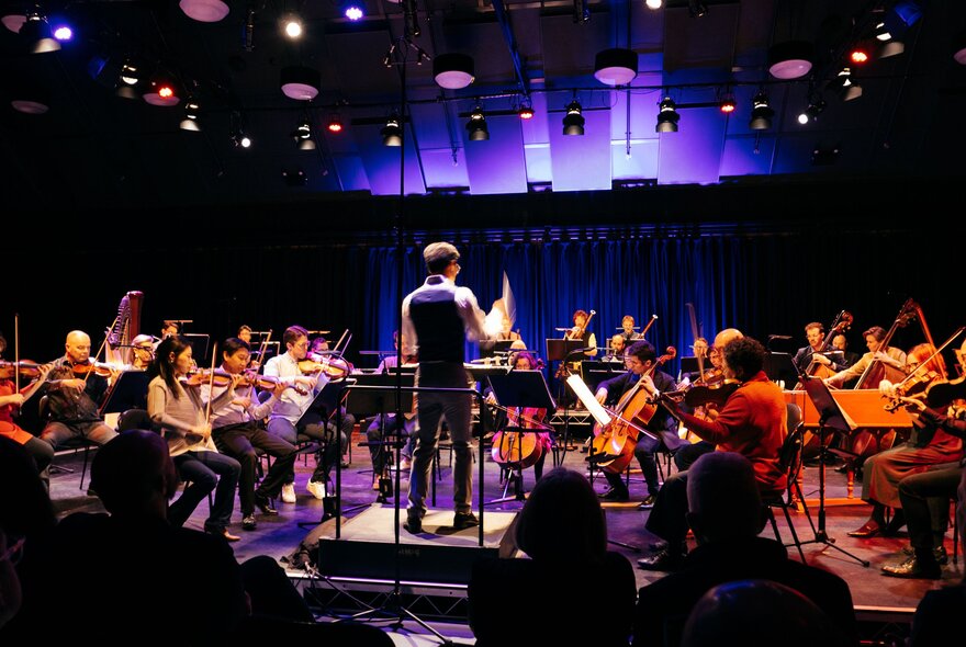 Orchestra Victoria performing in a small space with dim lights glowing purple and red. 