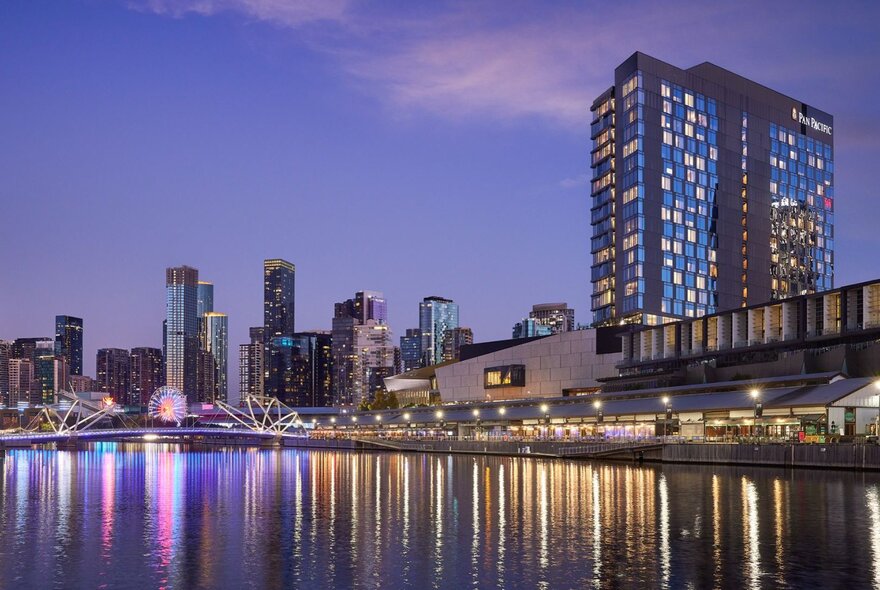 High-rise hotel positioned beside the Yarra River with lights reflected in the water at dusk.
