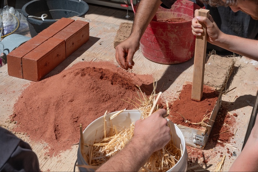 Hands making earth blocks out of red dirt. 