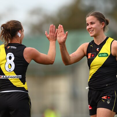 Two Richmond AFLW players celebrating with a high-five in their yellow and black guernseys.