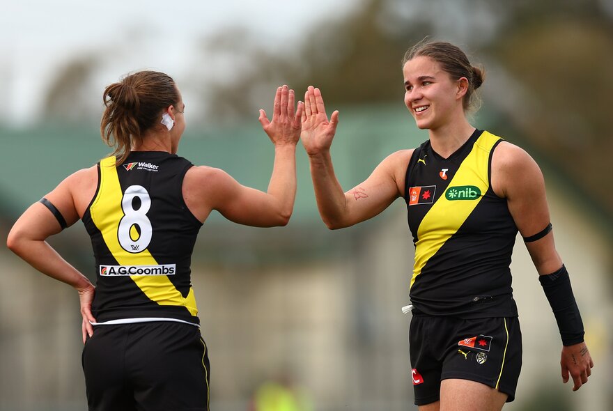 Two Richmond AFLW players celebrating with a high-five in their yellow and black guernseys.