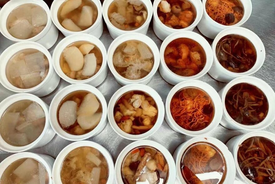 Rows and rows of white bowls filled with Asian soups, stews and dumplings.