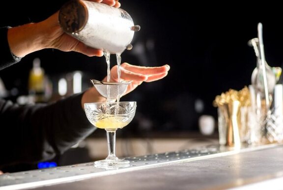 Bar tender pouring a tequila cocktail into a stemmed glass with a strainer.