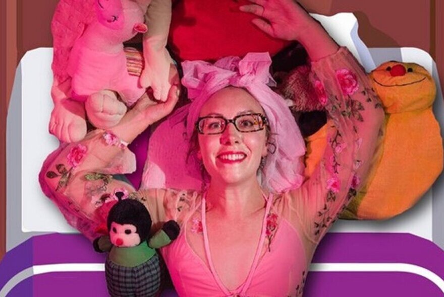 Looking down at a smiling performer lying on a bed, surrounded by soft toys and pillows.