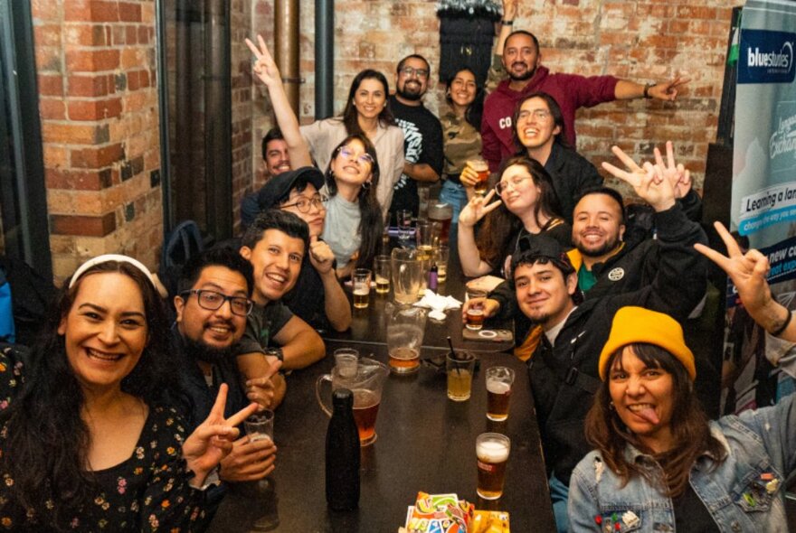 A very happy group of people in a bar posing for a photo at a long table.