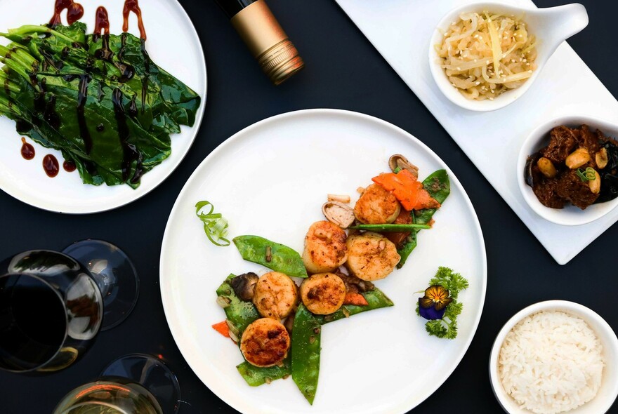 Bird's-eye view of a number of dishes, including rice, noodles and Chinese greens.