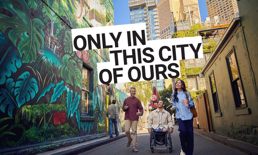 Three friends looking at street art in a laneway, one is using a wheechair. Text overlay reads 'only in this city of ours'.