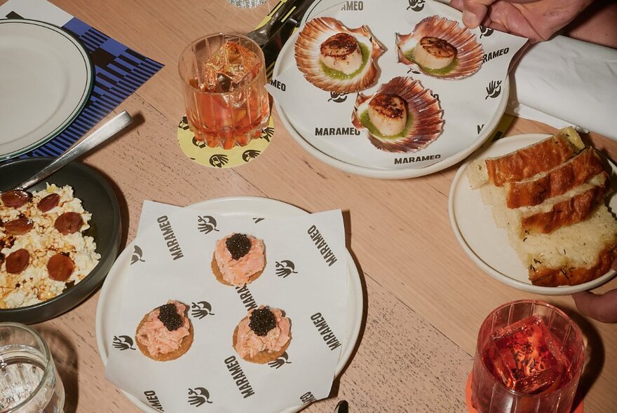 A selection of small snacks and canapes on plates, with drinks, on a restaurant dining table.