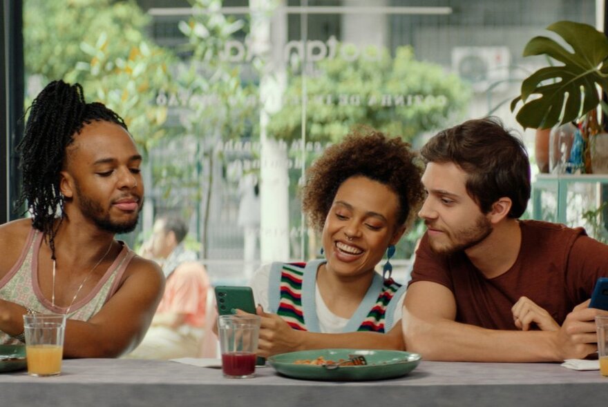 Three friends who are looking at something together in a cafe setting. 