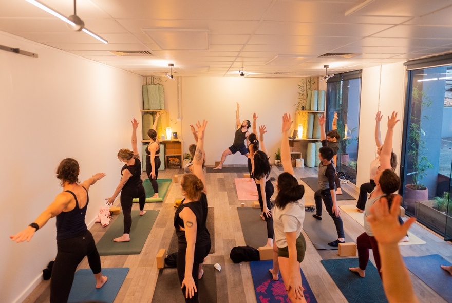 People attending a yoga class with mats in a room with large windows and bright lighting.