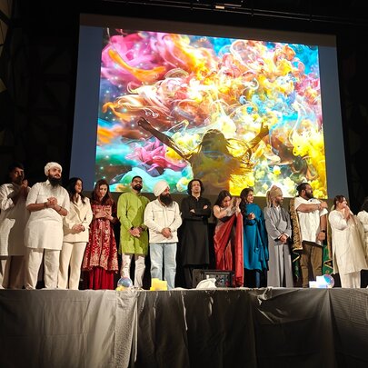An event on a stage, featuring a diverse group of individuals dressed in varied attire standing in a row, with a large screen behind them.